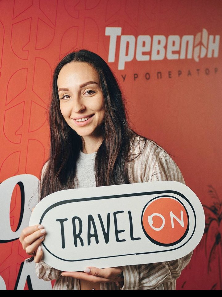 Анастасія Василенко з табличкою TravelON на тлі стіни з логотипом Тревелон