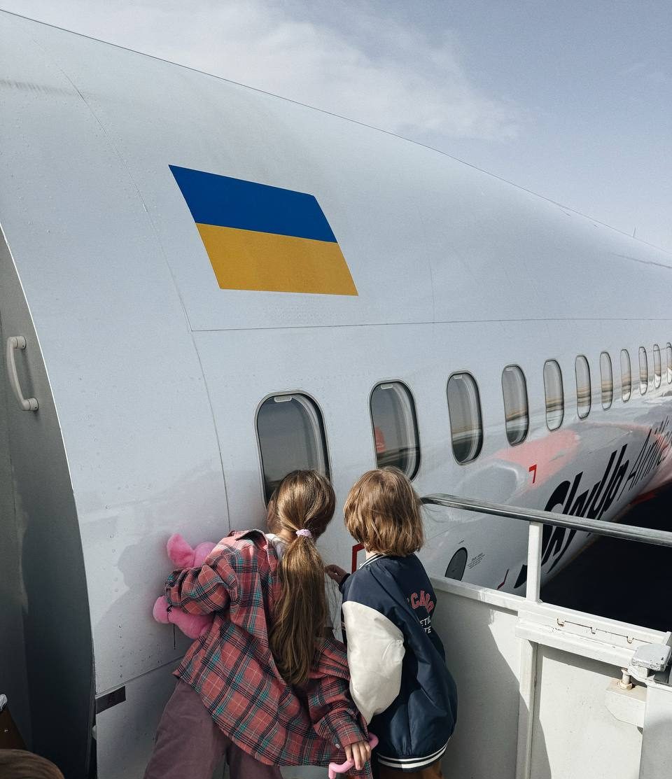 Двоє дітей біля трапа літака з українським прапором на борту